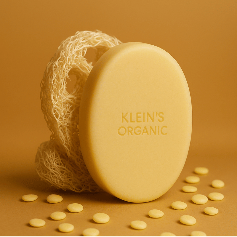 Kleins Organic moisturisng body butter standing next to a luther sponge surrounded by light orange background.