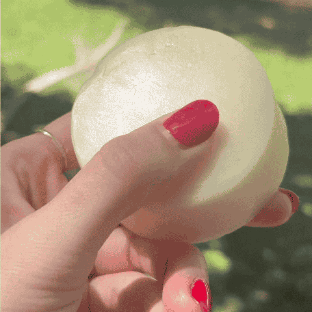 Hand holding a hard solid conditioner bar with red nail polish against a blurred green background